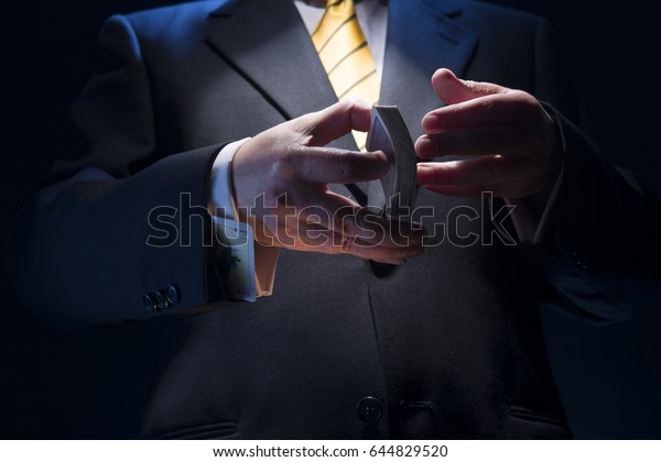 The man in a suit shuffles cards, in his sleeve he\
has a diamond ace