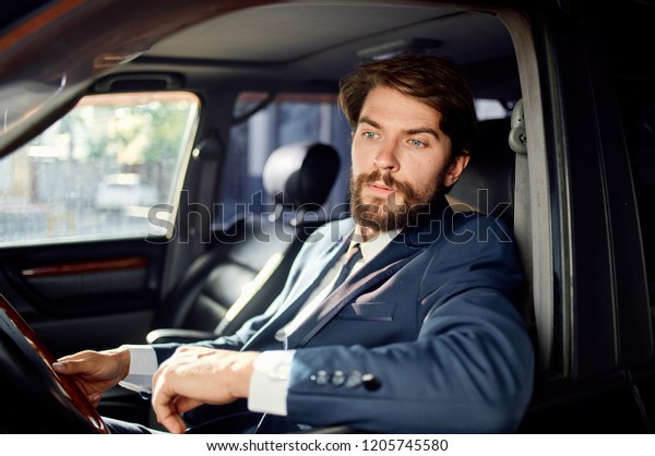 man in a suit sits behind\
the wheel of a car and looks into the camera                       \
       