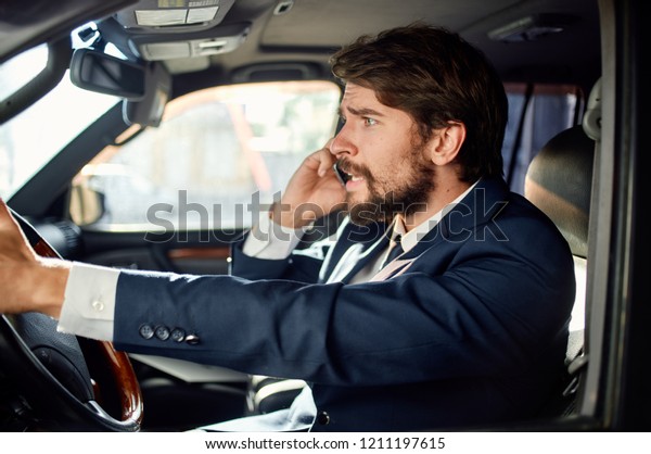man in a suit sits behind\
the wheel in the car and talking on the phone                      \
       