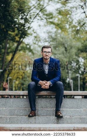 A man in a suit is sitting on a bench in the park