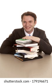 A man in a suit sitting over a stack of books smiling.
