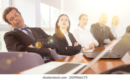 Man in suit sleeping on chair beside his colleagues during conference in meeting room. - Powered by Shutterstock