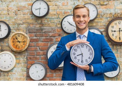 Man in suit standing near wall with clocks