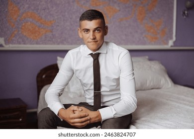 A man in a suit and tie is sitting on a bed. He is wearing a tie and a white shirt - Powered by Shutterstock