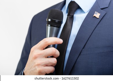 Man In Suit With Tie And USA Flag Pin On Chest Holding Microphone In Hand