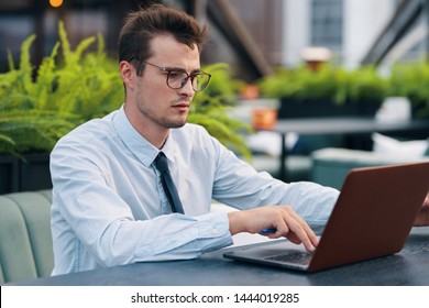 A man in a suit types text on a laptop keyboard and sits at a table in a cafe - Shutterstock ID 1444019285