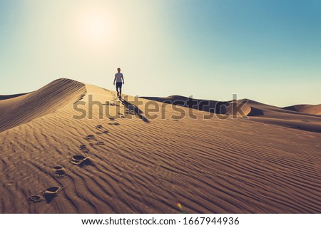 Man in summer clothes with sunglasses is going down the red dune tracing his footprints during sunny day in UAE Liwa desert, at the beautiful rippled sand 