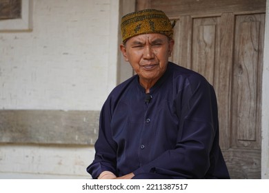 A Man In Sundanese Clothes Is Relaxing In The Yard Of A Traditional House. Using A Batik Headband. TASIKMALAYA, WEST JAVA - Des 08, 2021 