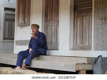 A Man In Sundanese Clothes Is Relaxing In The Yard Of A Traditional House. Using A Batik Headband. TASIKMALAYA, WEST JAVA - Des 08, 2021 