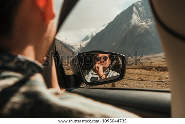 man in sunglasses looking at the mountains\
with car window reflected in the\
mirror