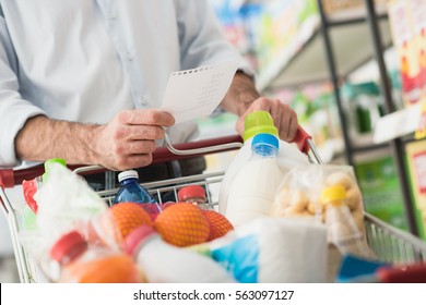 Man At The Supermarket Shopping With A Grocery List And Pushing A Full Cart, Lifestyle And Retail Concept