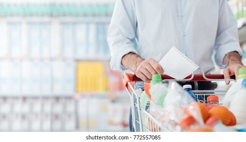 Man At The Supermarket Shopping With A Grocery List And Pushing A Full Cart, Lifestyle And Retail Concept