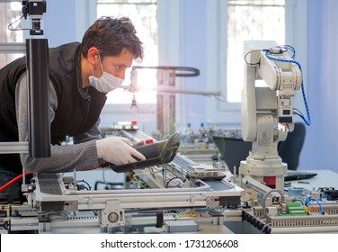 Man with surgical mask on face against COVID-19 ( Coronavirusis ) programming robot arm with control panel which is integrated on smart factory production line. industry 4.0 automation line. - Shutterstock ID 1731206608