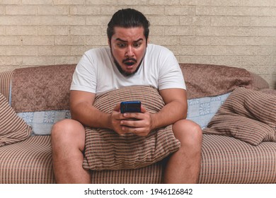 A man is surprised by a social media post or other related topic on the phone. Sitting on a couch at home during day off.