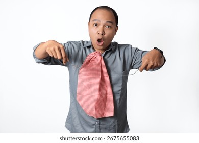 A man with a surprised expression, wearing a gray shirt and a red and white checkered napkin tied around his neck, is holding a fork and knife.