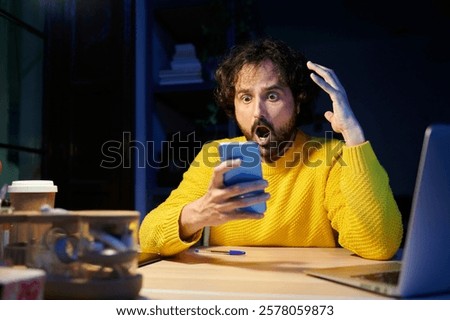 Man with a surprised face using mobile phone in the office at night.