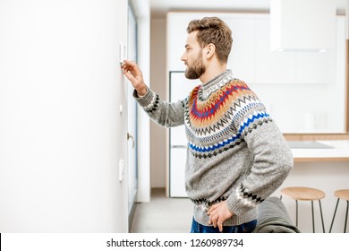 Man In Sweater Adjusting Room Temperature With Electronic Thermostat At Home