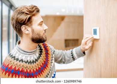 Man In Sweater Feeling Cold Adjusting Room Temperature With Electronic Thermostat At Home