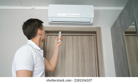 Man Sweats And Turns On Air Conditioner With Remote Control In Hot Room. Sweaty Guy After Feeling Cool Air From Cooling Device Smiles And Relaxes