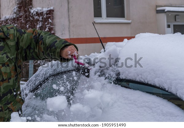 A man sweeps\
snow from car with a hand brush\
