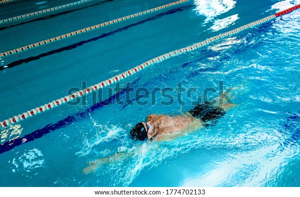 Man swimmer is swimming\
in the pool, backstroke technique swimming. Shot of swim in motion,\
top view