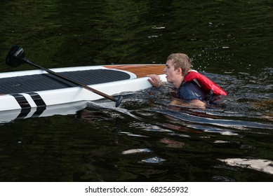 Man Swimming Back To Stand Up Paddle Board, Muskoka, Ontario, Canada.