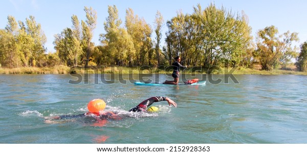 Man swimming on a river, guided by a\
SUP, open water competition, Marathon\
swimming
