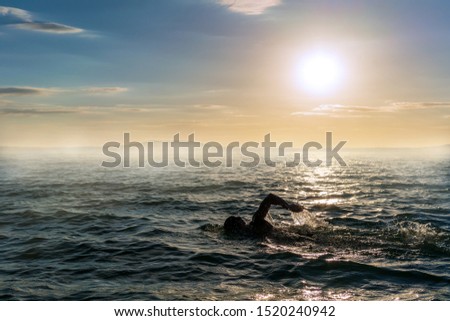 Man swimming in open water during a misty sunset