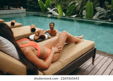 Man in swimming pool with woman relaxing on deckchair at poolside. Couple enjoying at holiday resort. - Powered by Shutterstock