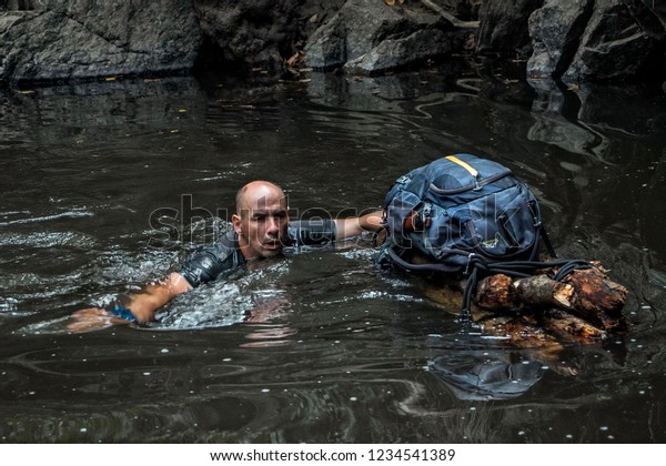 A man is\
swimming in a river and at the same time supporting a hand-made\
improvised raft with his backpack. Concept of survival and\
exploration in the wild. Man vs\
wild.