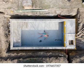 Man In Swimming Trunks Lies In Not Yet Finished Pool On A Floating Tire And Takes Selfie With Drone