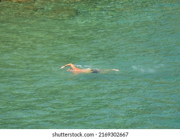 A Man Swims Crawl Style In Turquoise Water On Crete, Greece