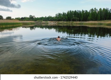  A man swims in a deserted forest lake before the rain in Ukraine. Circles on the water. Copy space. - Powered by Shutterstock