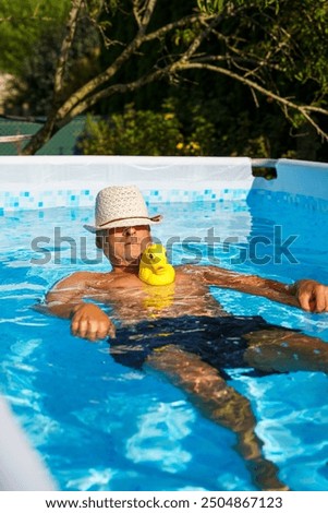 Ein Mann mit Sonnenhut und einer gelben Gummiente in einem Pool.