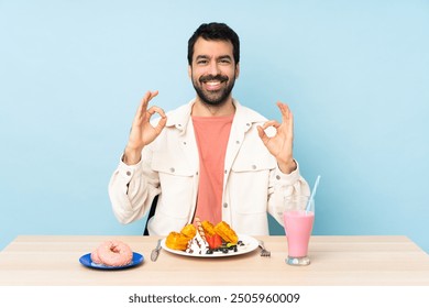 Man at a table having breakfast waffles and a milkshake showing an ok sign with fingers - Powered by Shutterstock