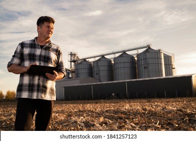 Man with tablet in his hands standing in front of agricultural silos 