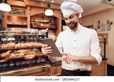 A man with a tablet in his hands stands in the middle of the bakery. Young chef in a new bakery with a tablet.  - Powered by Shutterstock