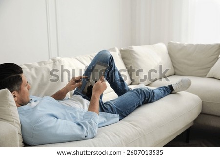 Man with tablet lying on comfortable sofa in living room