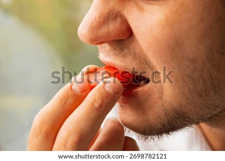 A man takes a bite out of a slice of red tomato, organic fresh food. Plum tomato