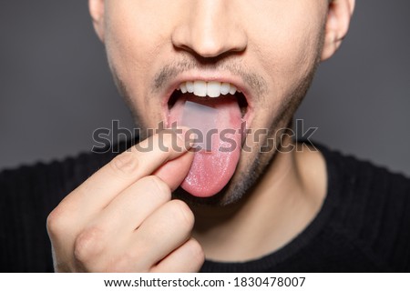 man takes breath stripes on his tounge that refreshes breath in mouth, removes smell and kills bacteria and germs