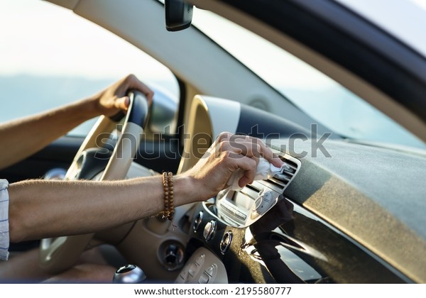 Man takes care of work of air ventilation system\
when driving car sitting at driver seat and controlling steering\
wheel. Hand of driver wipes dust from panel vent for air flow\
during road trip