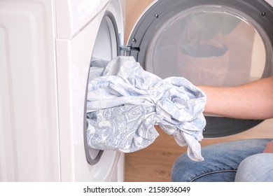 A man takes dried bed linen out of the dryer. Dryer machine in the house.