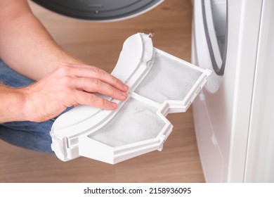 A man takes a lint filter out of the dryer and cleans it from dust, lint, hair, wool.