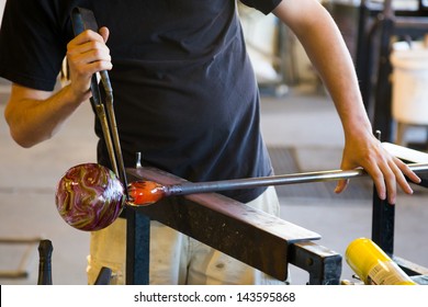 A man takes motlen glass and shapes it using some specialized tools for glassblowing art. - Powered by Shutterstock