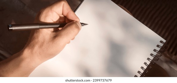 A man takes notes, sketches or makes a plan on a blank white sheet of paper in an album, a businessman, aspiring writer or student holds a notepad and a black pen in his hands, close-up top view. - Powered by Shutterstock