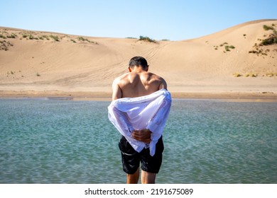 A Man Takes Off His White Shirt On The Sea With His Back To The Shore