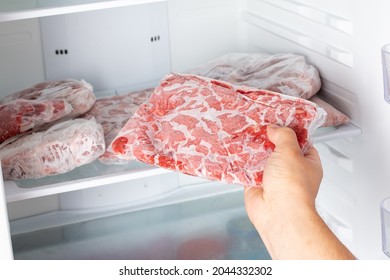 The Man takes out a bag of frozen meat from the freezer in the kitchen at home. Frozen food