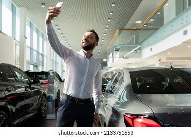 A Man Takes A Picture Of Himself On The Phone In A Car Dealership Against The Background Of A New Car