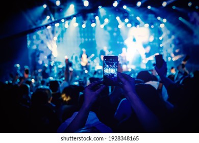 Man takes a picture of the show at the concert hall using a smartphone - Powered by Shutterstock