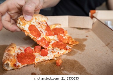 Man takes a slice of pizza from a cardboard box close-up.